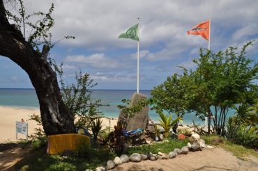 Facing the lifesavers’ building in Boucan Canot, the green surfing flag is raised for the first time, meaning that marine activities are allowed within the nets. In the foreground, a memorial was built for several victims of shark attacks © Andy Guinand / OCEAN71 Magazine